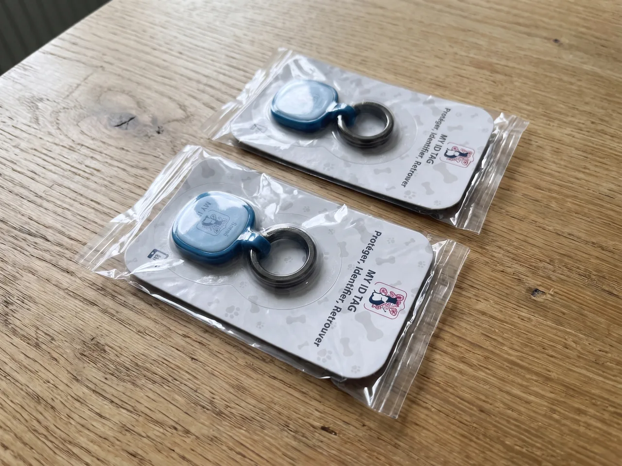 Deux médailles MyIDTag dans leur blister, posées sur une table en bois.