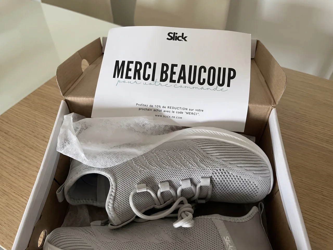La basket Slick finie, maille grise et semelle blanche, posée sur un établi d'usine de chaussures.
