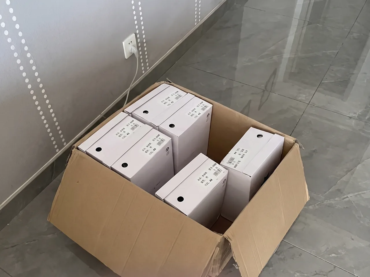 Contrôle avant chargement : carton ouvert de baskets sous sachet sur une palette, vérification sur tablette.